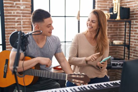 Photo for Man and woman musicians having classic guitar lesson using smartphone at music studio - Royalty Free Image