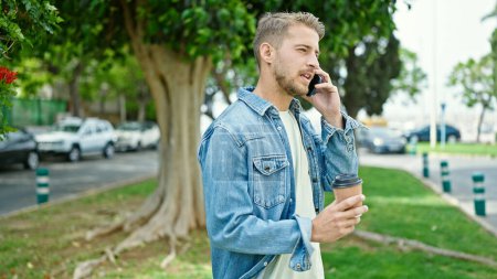 Téléchargez les photos : Jeune homme caucasien parlant sur smartphone boire du café au parc - en image libre de droit