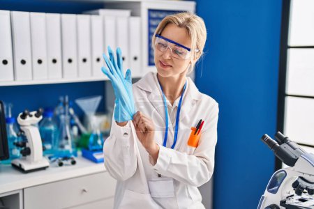 Téléchargez les photos : Jeune femme blonde scientifique debout avec les bras croisés geste au laboratoire - en image libre de droit