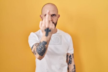 Téléchargez les photos : Young hispanic man with tattoos standing over yellow background showing middle finger, impolite and rude fuck off expression - en image libre de droit