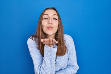 Photo for Young woman standing over blue background looking at the camera blowing a kiss with hand on air being lovely and sexy. love expression. - Royalty Free Image