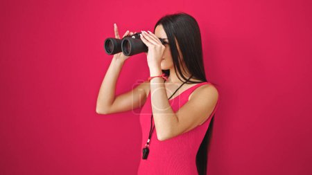Téléchargez les photos : Jeune belle femme hispanique sauveteur à l'aide de jumelles avec expression détendue sur fond rouge isolé - en image libre de droit