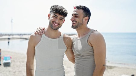 Foto de Dos hombres pareja sonriendo confiado abrazándose en la orilla del mar - Imagen libre de derechos