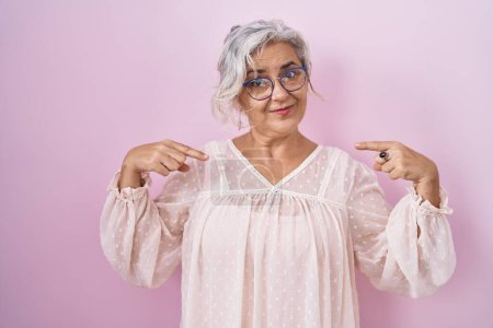 Foto de Middle age woman with grey hair standing over pink background looking confident with smile on face, pointing oneself with fingers proud and happy. - Imagen libre de derechos