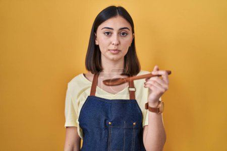 Foto de Chica hispana comiendo cuchara de madera saludable relajado con expresión seria en la cara. simple y natural mirando a la cámara. - Imagen libre de derechos