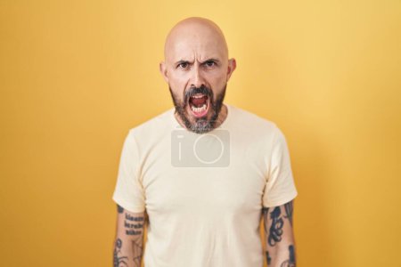 Téléchargez les photos : Homme hispanique avec des tatouages debout sur fond jaune en colère et fou hurlant frustré et furieux, criant de colère. rage et concept agressif. - en image libre de droit