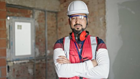 Photo for Young latin man builder standing with relaxed expression and arms crossed gesture at construction site - Royalty Free Image