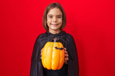 Photo for Little hispanic boy wearing a cape and holding halloween pumpkin thinking attitude and sober expression looking self confident - Royalty Free Image