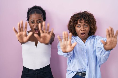 Téléchargez les photos : Deux femmes africaines debout sur fond rose faisant un geste d'arrêt avec les paumes des mains, expression de colère et de frustration - en image libre de droit