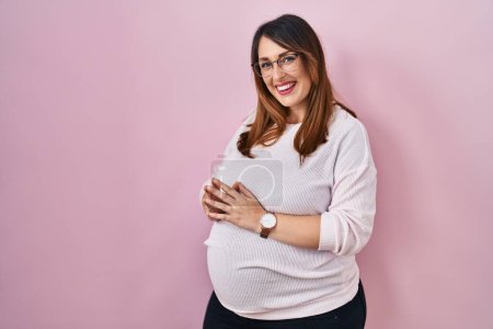 Téléchargez les photos : Femme enceinte debout sur fond rose mains ensemble et doigts croisés souriant détendu et joyeux. succès et optimisme - en image libre de droit