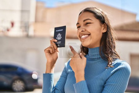 Foto de Joven mujer afroamericana sonriendo confiada sosteniendo el pasaporte de los estados unidos en la calle - Imagen libre de derechos