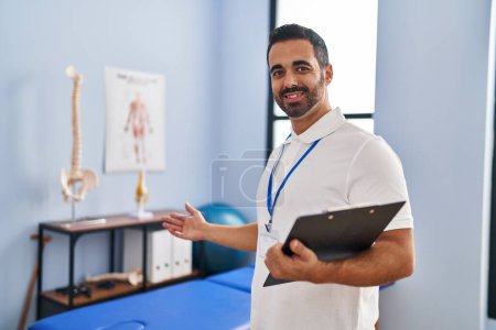 Photo for Young hispanic man physiotherapist smiling confident holding clipboard at rehab clinic - Royalty Free Image