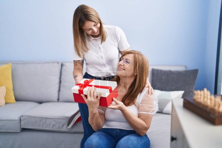 Photo for Mother and daughter surprise with gift hugging each other at home - Royalty Free Image