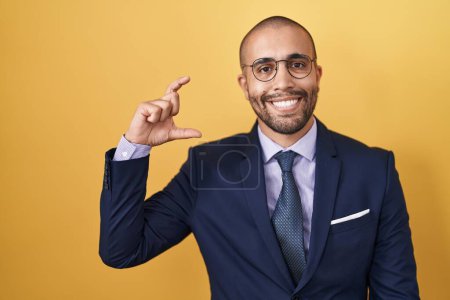 Téléchargez les photos : Homme hispanique avec barbe portant costume et cravate sourire et geste confiant avec la main faisant signe de petite taille avec les doigts regardant et la caméra. concept de mesure. - en image libre de droit