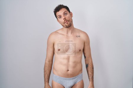 Photo for Young hispanic man standing shirtless wearing underware making fish face with lips, crazy and comical gesture. funny expression. - Royalty Free Image