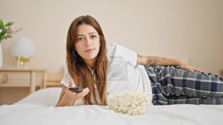 Foto de Joven hermosa mujer hispana viendo la televisión acostada en la cama con expresión aburrida en el dormitorio - Imagen libre de derechos
