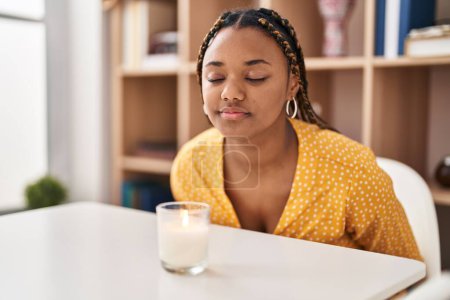 Foto de Mujer afroamericana sentada en la mesa oliendo vela aromática en casa - Imagen libre de derechos