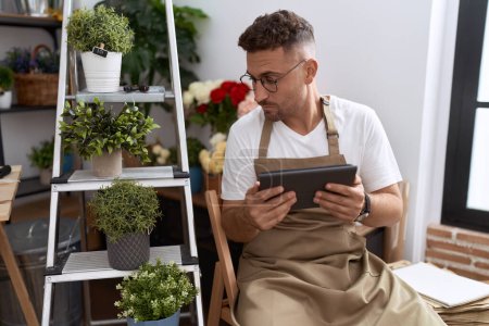 Téléchargez les photos : Young hispanic man florist using touchpad at flower shop - en image libre de droit
