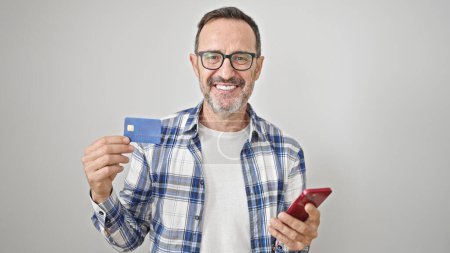 Téléchargez les photos : Homme du moyen âge en utilisant smartphone et carte de crédit sur fond blanc isolé - en image libre de droit