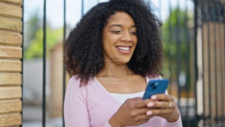 Foto de Mujer afroamericana usando smartphone sonriendo en la calle - Imagen libre de derechos