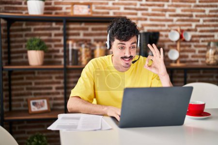 Photo for Hispanic man wearing call center agent headset working from home doing ok sign with fingers, smiling friendly gesturing excellent symbol - Royalty Free Image