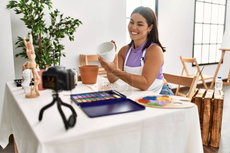 Foto de Joven hermosa mujer hispana artista grabación vídeo pintura arcilla olla en estudio de arte - Imagen libre de derechos
