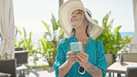 Photo for Middle age grey-haired woman tourist smiling confident using smartphone at coffee shop terrace - Royalty Free Image