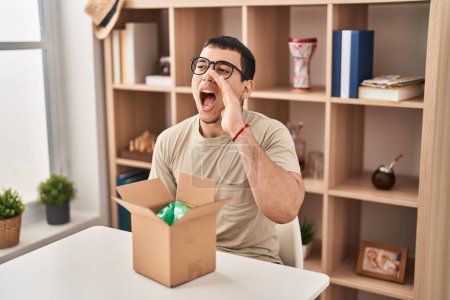 Photo for Young arab man with open gift in cardboard box clueless and confused with open arms, no idea and doubtful face. - Royalty Free Image