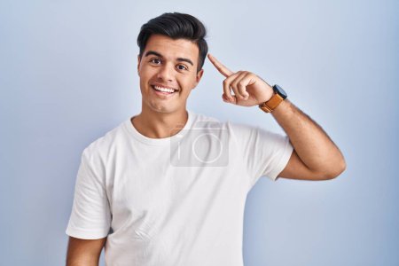 Téléchargez les photos : Homme hispanique debout sur fond bleu souriant pointant vers la tête avec un doigt, grande idée ou pensée, bonne mémoire - en image libre de droit