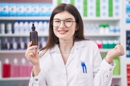 Photo for Young caucasian woman working at pharmacy drugstore holding serum screaming proud, celebrating victory and success very excited with raised arm - Royalty Free Image