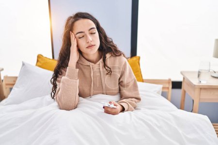 Photo for Young hispanic woman sitting on bed suffering for headache at bedroom - Royalty Free Image