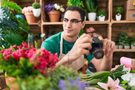 Photo for Young hispanic man florist holding professional camera at flower shop - Royalty Free Image