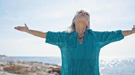 Foto de Mujer de pelo gris de mediana edad respirando con los brazos abiertos en la playa - Imagen libre de derechos