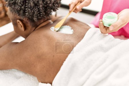Photo for African american woman lying on table having back massage using cream at beauty salon - Royalty Free Image