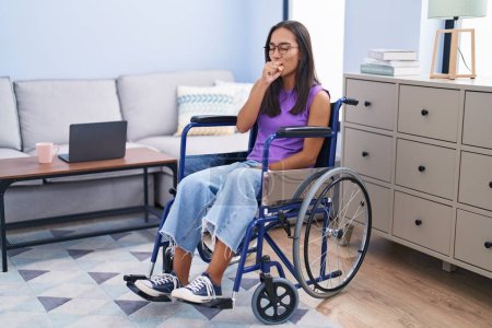 Foto de Mujer hispana joven sentada en silla de ruedas en casa sintiéndose mal y tosiendo como síntoma de resfriado o bronquitis. concepto de atención sanitaria. - Imagen libre de derechos