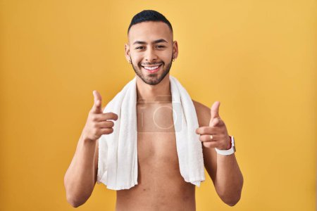Photo for Young hispanic man standing shirtless with towel pointing fingers to camera with happy and funny face. good energy and vibes. - Royalty Free Image