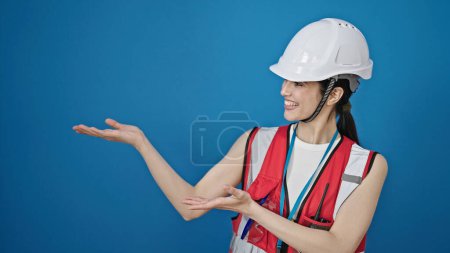 Photo for Young beautiful hispanic woman builder smiling confident presenting over isolated blue background - Royalty Free Image