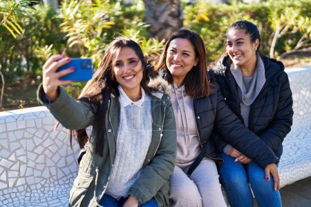 Photo for Three woman mother and daughters making selfie by smartphone sitting on bench at park - Royalty Free Image