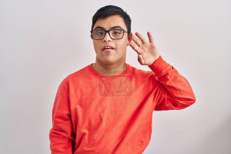 Photo for Young hispanic man with down syndrome standing over white background smiling with hand over ear listening and hearing to rumor or gossip. deafness concept. - Royalty Free Image