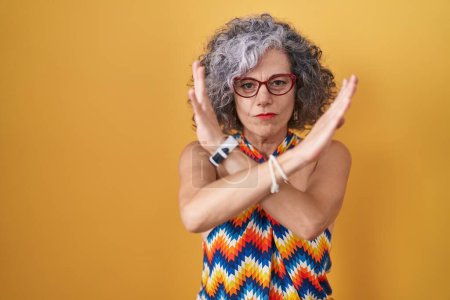 Photo for Middle age woman with grey hair standing over yellow background rejection expression crossing arms doing negative sign, angry face - Royalty Free Image