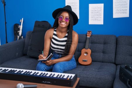 Foto de Afro-americana mujer músico sonriendo confiado componiendo canción en estudio de música - Imagen libre de derechos
