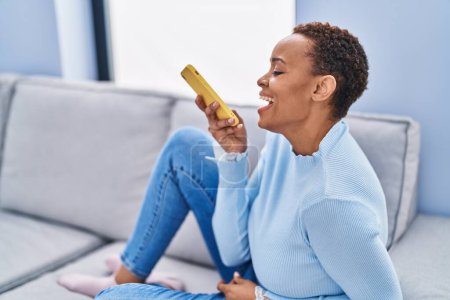 Téléchargez les photos : Femme afro-américaine parlant sur smartphone assis sur le canapé à la maison - en image libre de droit