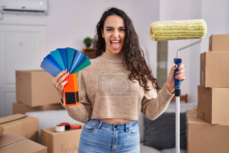 Photo for Young brunette woman moving to a new home painting walls sticking tongue out happy with funny expression. - Royalty Free Image