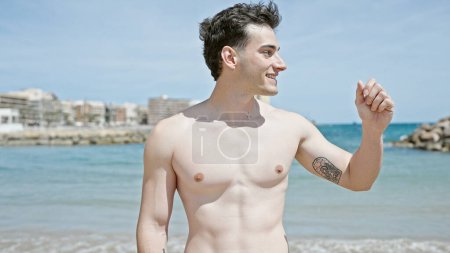 Foto de Joven turista hispano sonriendo confiado de pie en la playa - Imagen libre de derechos