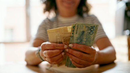 Hispanische Frau mittleren Alters zählt zu Hause echte brasilianische Banknoten