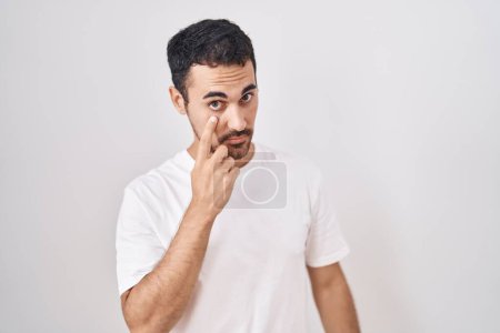 Foto de Hombre hispano guapo de pie sobre fondo blanco apuntando al ojo observándote gesto, expresión sospechosa - Imagen libre de derechos