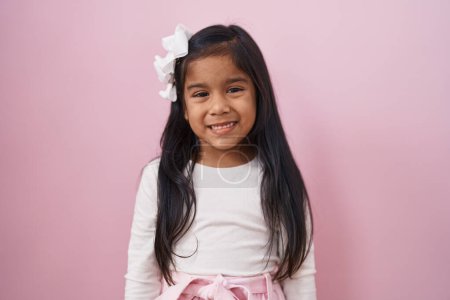 Téléchargez les photos : Petite fille hispanique debout sur fond rose regardant positif et heureux debout et souriant avec un sourire confiant montrant les dents - en image libre de droit