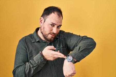 Photo for Plus size hispanic man with beard standing over yellow background in hurry pointing to watch time, impatience, upset and angry for deadline delay - Royalty Free Image