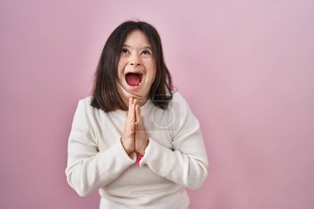 Photo for Woman with down syndrome standing over pink background begging and praying with hands together with hope expression on face very emotional and worried. begging. - Royalty Free Image