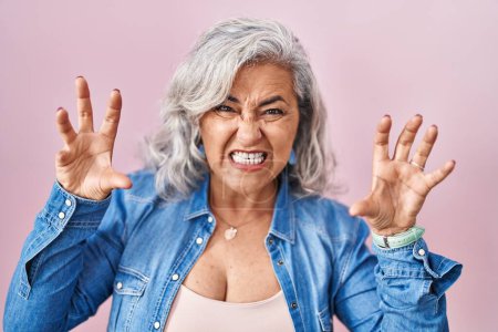 Photo for Middle age woman with grey hair standing over pink background smiling funny doing claw gesture as cat, aggressive and sexy expression - Royalty Free Image